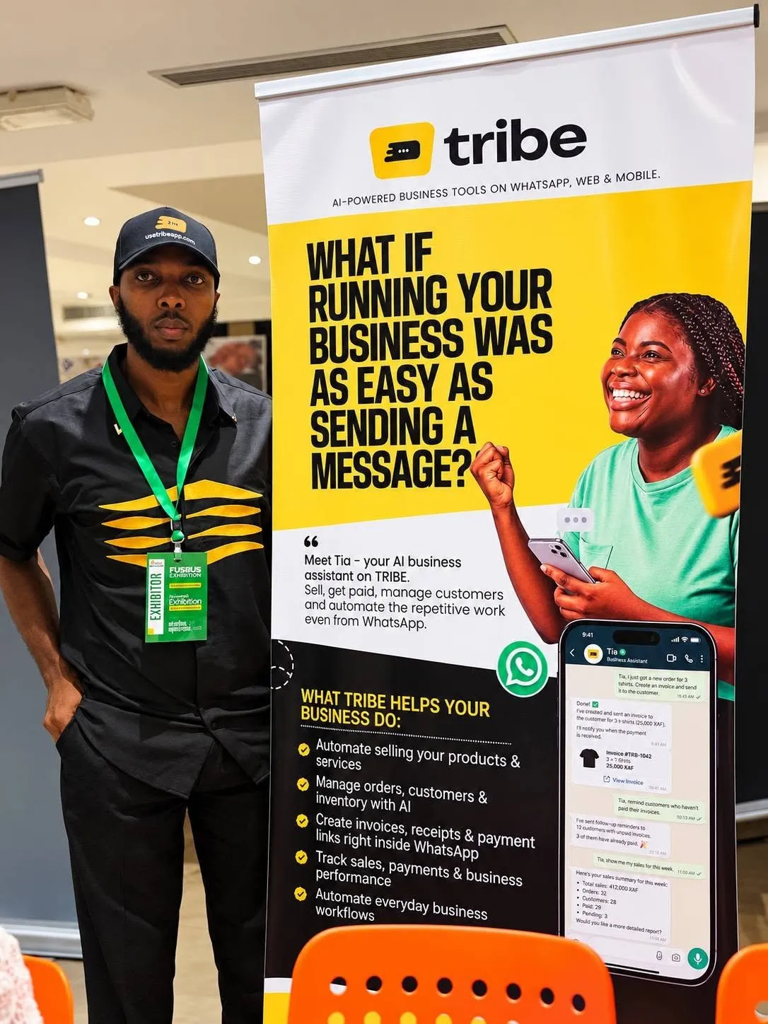 Emmanuel Cobbi standing beside a Tribe roll-up banner at a business exhibition.