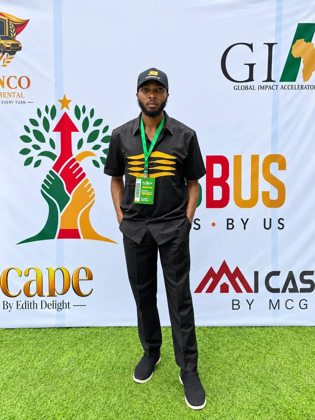 Emmanuel Cobbi standing in front of an event backdrop wearing an exhibitor badge.