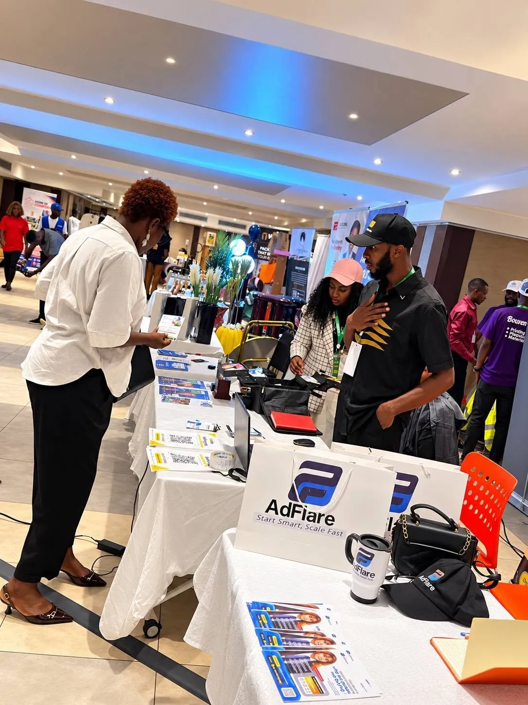 Emmanuel Cobbi at the Tribe exhibition stand, showing branded bags and printed material on the table.