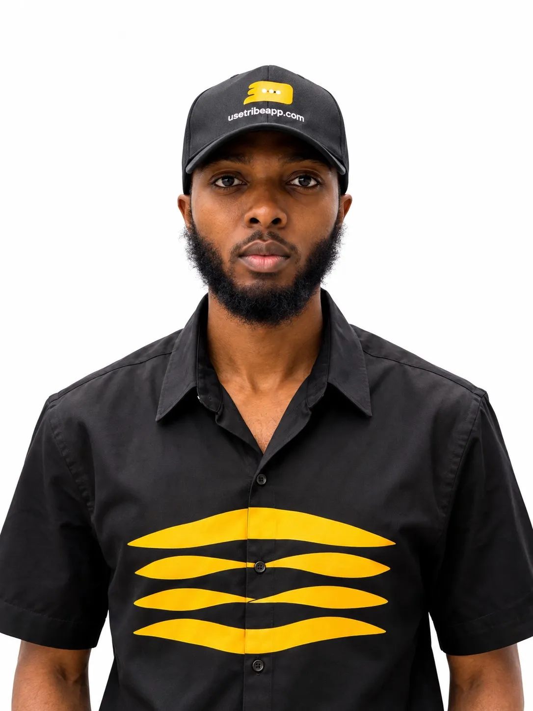 Studio photograph of Emmanuel Cobbi in a black Tribe cap and a black shirt carrying the yellow Tribe mark.